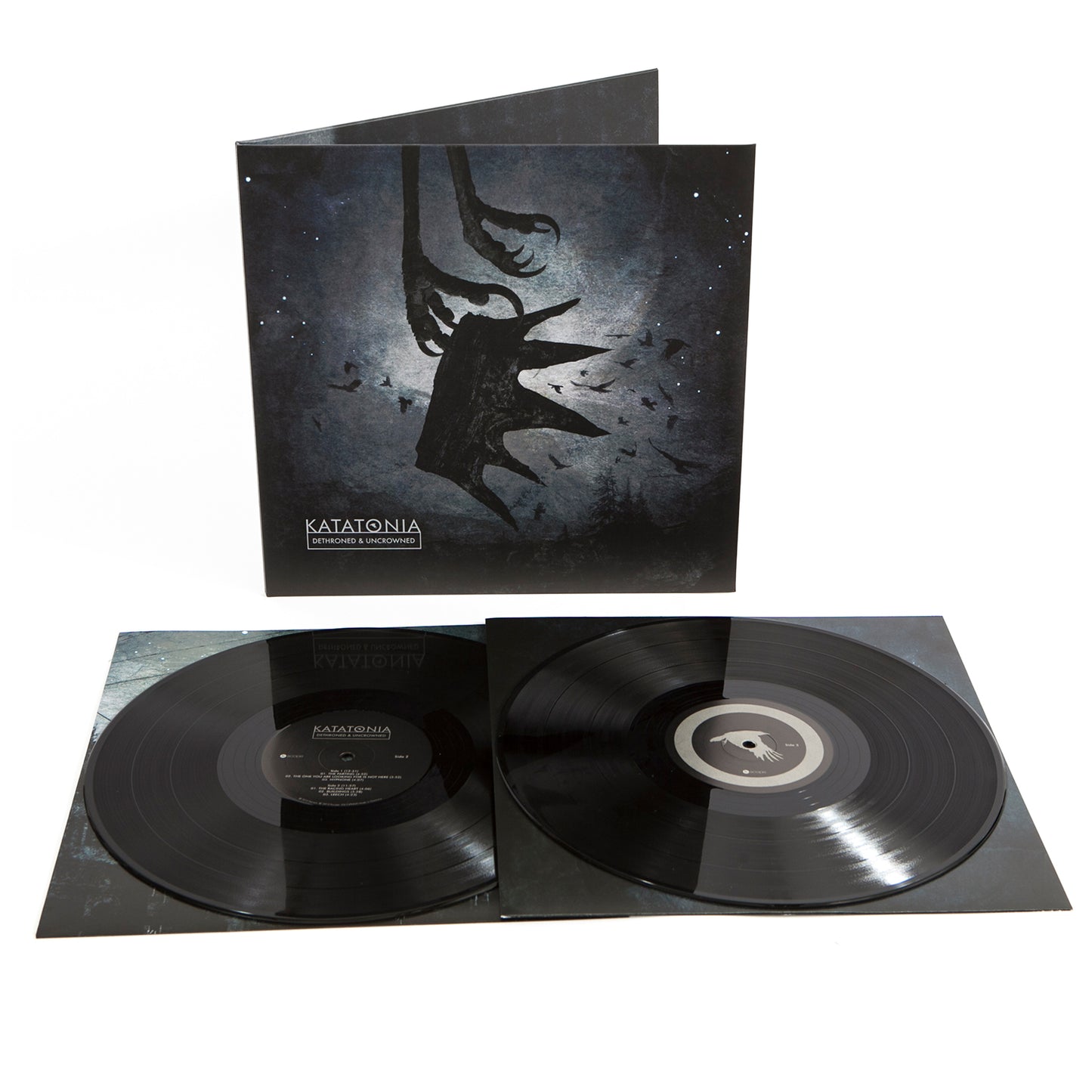 Katatonia’s Dethroned & Uncrowned vinyl set features two black records and a dark, atmospheric cover with a shadowy figure, birds, and abstract shapes—a haunting reimagining of Dead End Kings.