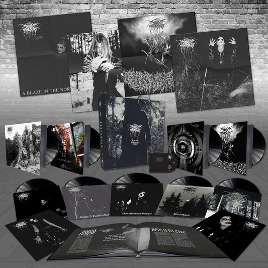 A collection of Darkthrone black metal vinyl records, CDs, and deluxe boxsets featuring dark, monochromatic artwork with band members, forests, and abstract designs, all arranged against a brick wall background.